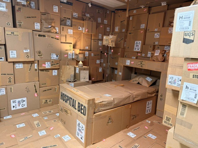 Cardboard room filled with stacked shipping boxes and a hospital bed labeled "Hospital Bed."