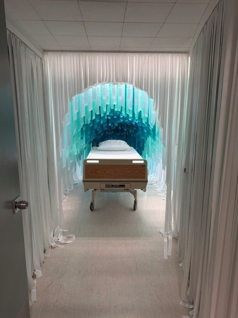 Hospital bed framed by a tunnel of cascading blue and white hanging fabric in an immersive installation at Hospital of Emotions.