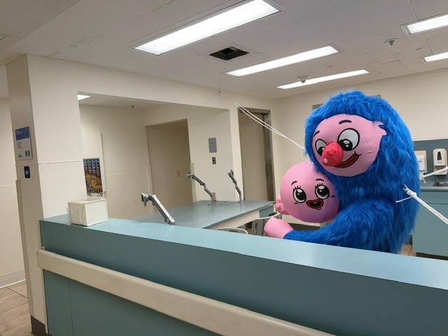 Blue furry cartoon-like figures embracing behind a former hospital reception desk.