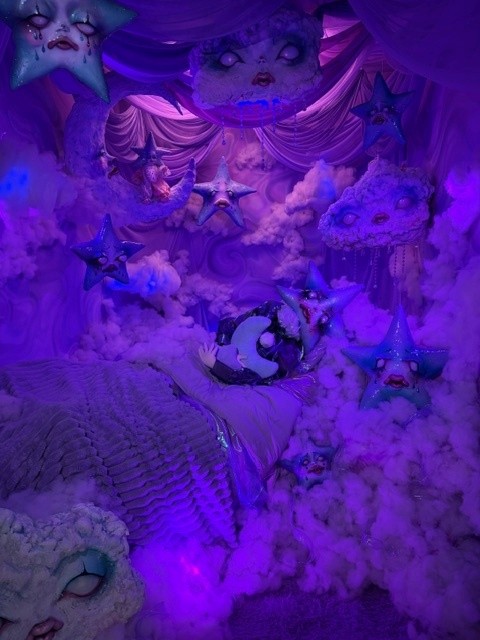 Dreamlike purple immersive installation filled with clouds, stars, and whimsical floating faces.