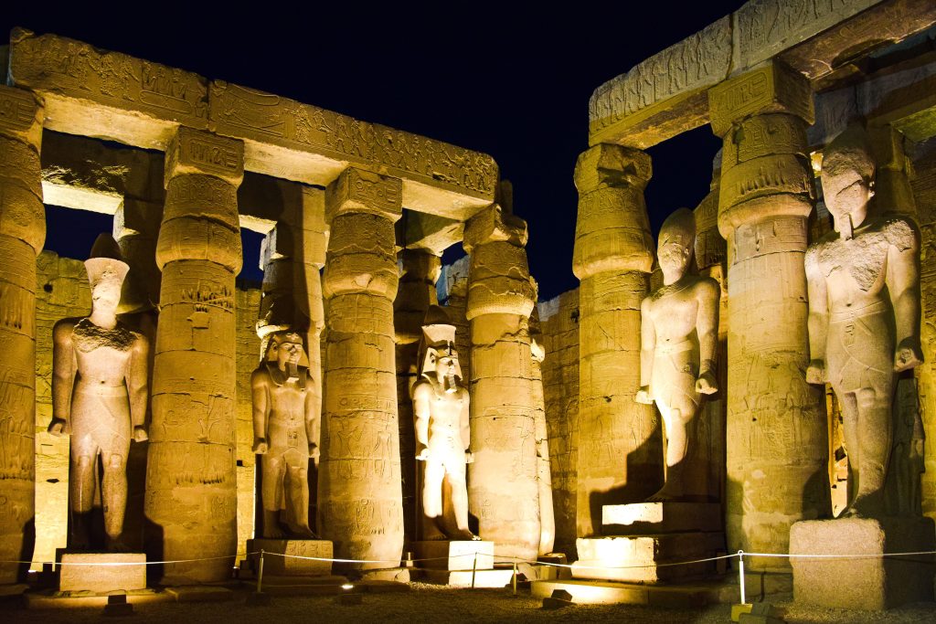 Massive ancient Egyptian statues and carved columns illuminated at Luxor Temple in Egypt at night.
