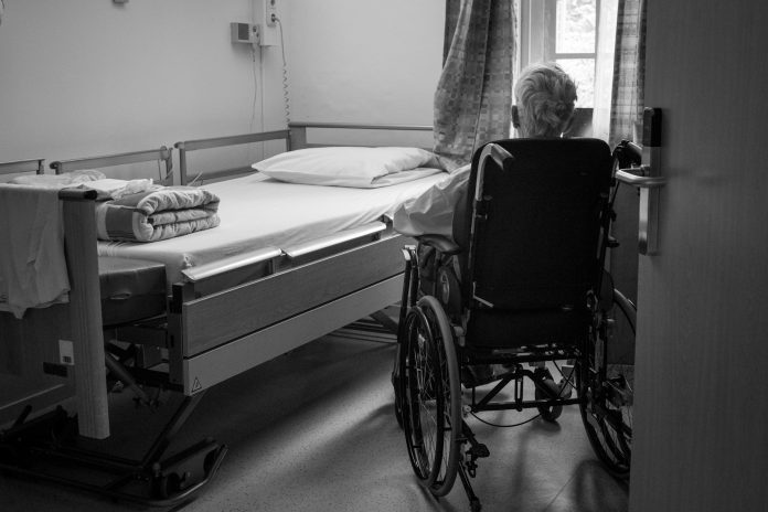 Older adult in a wheelchair beside a hospital bed, illustrating chronic illness and healthy aging