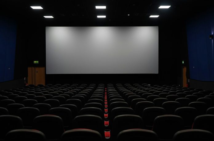 geoffrey-moffett-TFRezw7pQwI-unsplash Empty digital movie theater with rows of black seats facing a large cinema screen, representing modern film exhibition, digital theater distribution, and entertainment technology.