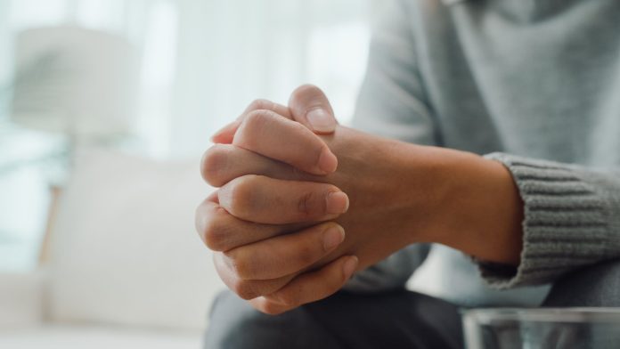 image Close-up of a person sitting with hands clasped together in a thoughtful or concerned pose, illustrating the topic of Canadian sexual assault law, consent, and legal rights.