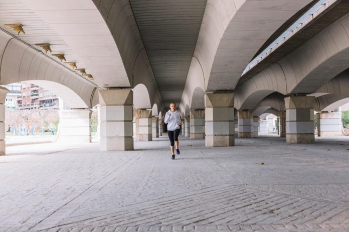Woman running beneath a large concrete bridge, illustrating the public space planned for the $62-million Sixth Street PARC in Los Angeles.