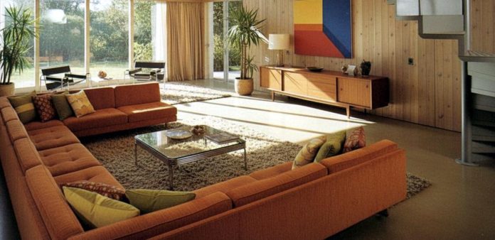 image 1970s-inspired living room with orange modular sofas, wood-paneled walls, shag rug and large windows.
