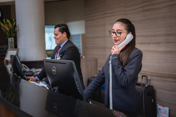 Hotel receptionist speaking on the phone at a front desk, representing transparency, customer service and protecting customer rights.