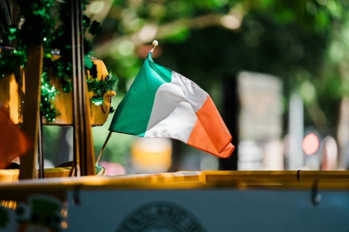 stewart-munro-6tvwN_GtBH0-unsplash Irish flag waving outdoors with a blurred green background.