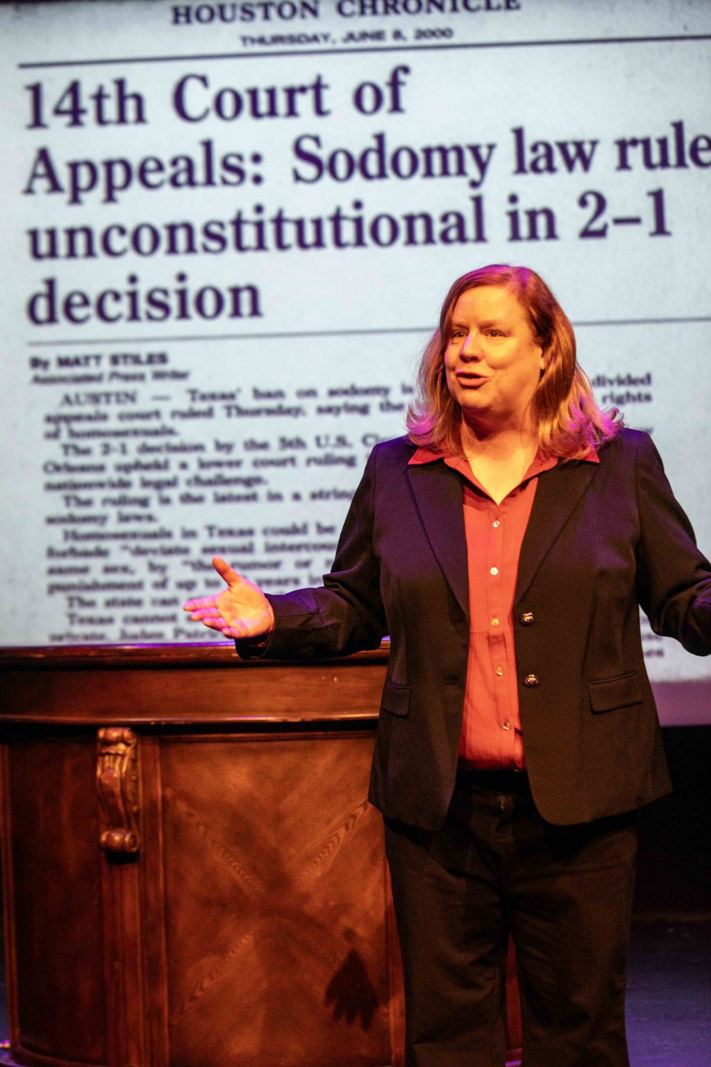 Scene from Texas Sodomy at Whitefire Theatre with a performer standing before a projected Houston Chronicle headline about Texas sodomy law.