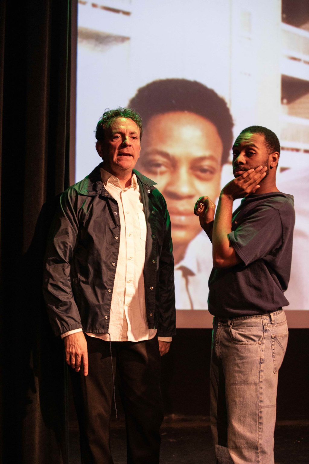Two performers in Texas Sodomy onstage in front of a projected portrait during the Whitefire Theatre production.