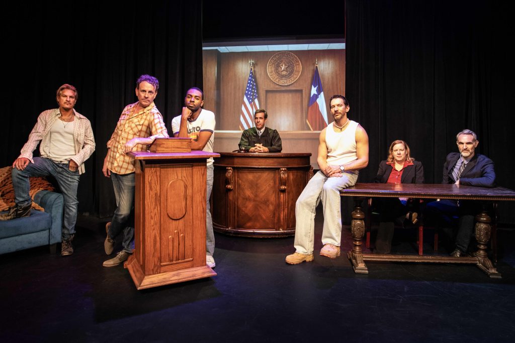 Cast of Texas Sodomy in a courtroom scene at Whitefire Theatre with American and Texas flags projected behind them.