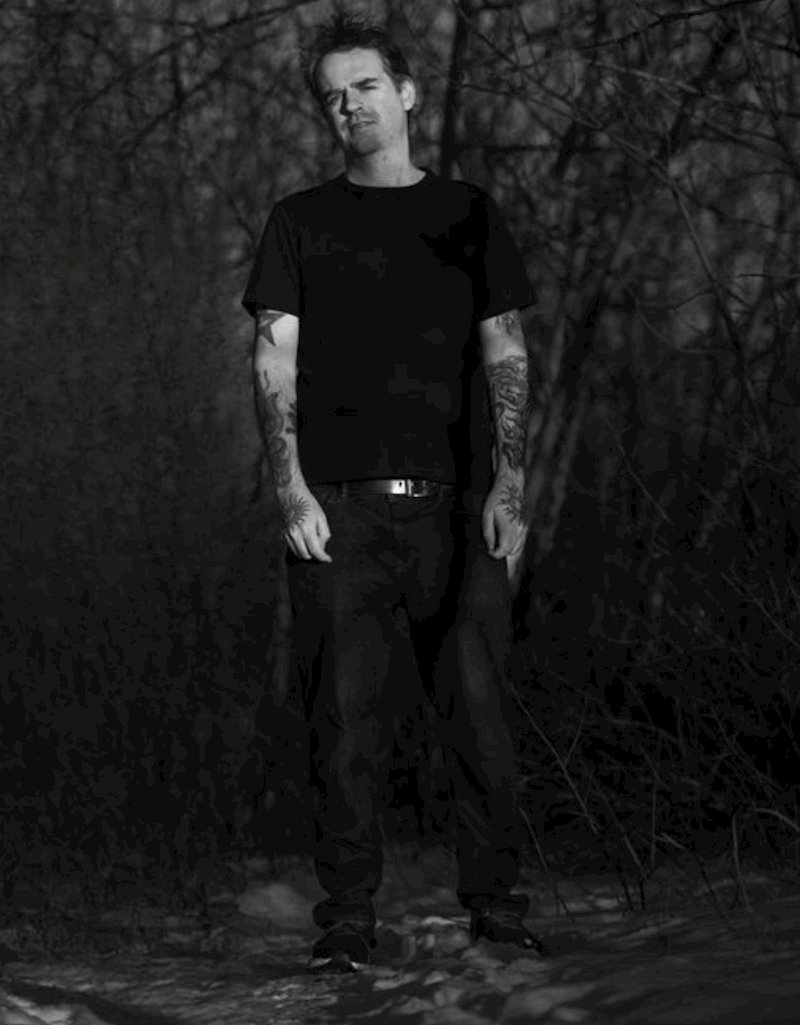 Stephen James Moore of Post Death Soundtrack wearing dark sunglasses against a dark backdrop.
