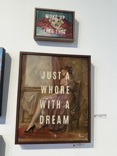 Two framed artworks combining vintage-style imagery with bold text, including “Woke Up Like This” and “Just a Whore With a Dream,” at Laluzapalooza 2026.