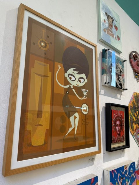 Retro-inspired artwork of a woman holding a cocktail, displayed alongside other colorful pieces at Laluzapalooza 2026.