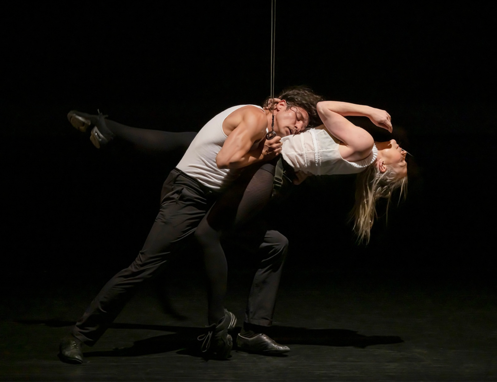 Luminario Ballet dancers performing an intense contemporary duet on a dark stage.