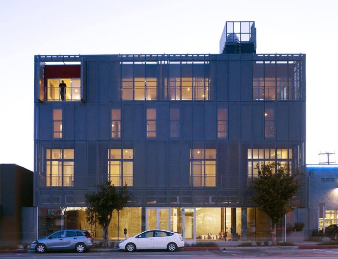 building noho sancturary Modern North Hollywood apartment building at dusk with illuminated windows and ground-floor storefronts.
