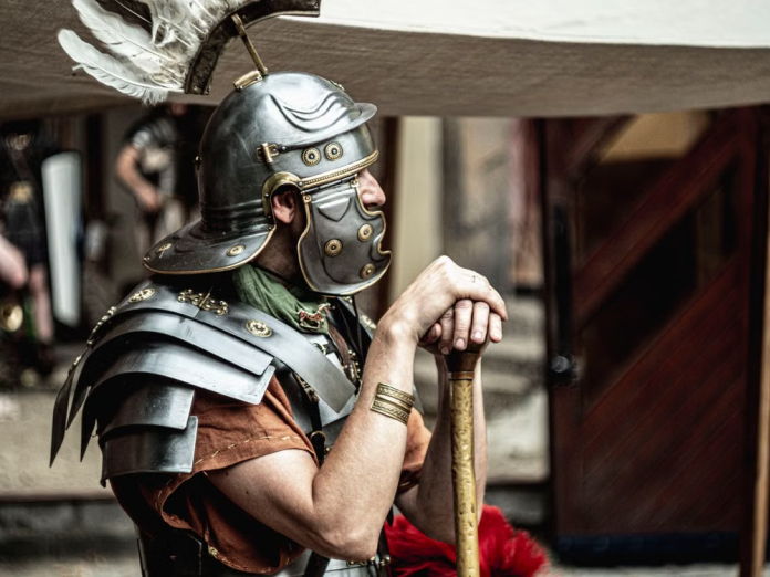 LARP player wearing detailed fantasy armor and helmet while resting on a weapon at a live action roleplay event.
