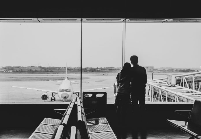 parentswatchingatairport Couple standing at an airport gate watching an airplane through terminal windows.