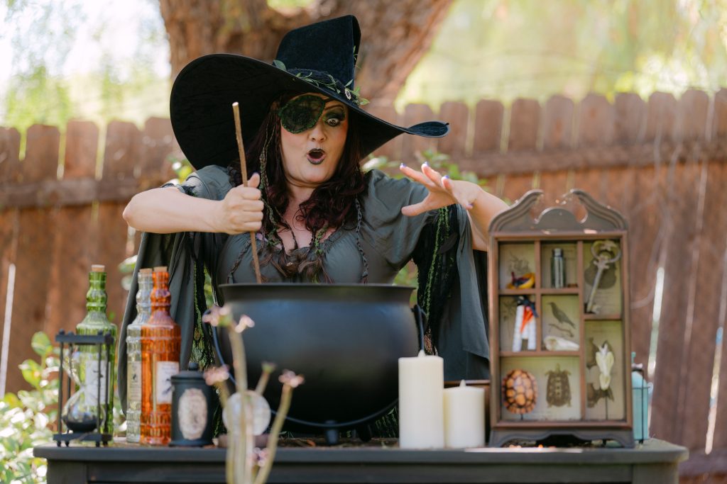 A witch character stirs a large cauldron during Heart to Art Productions’ immersive Fall Into Oz outdoor theatre experience.