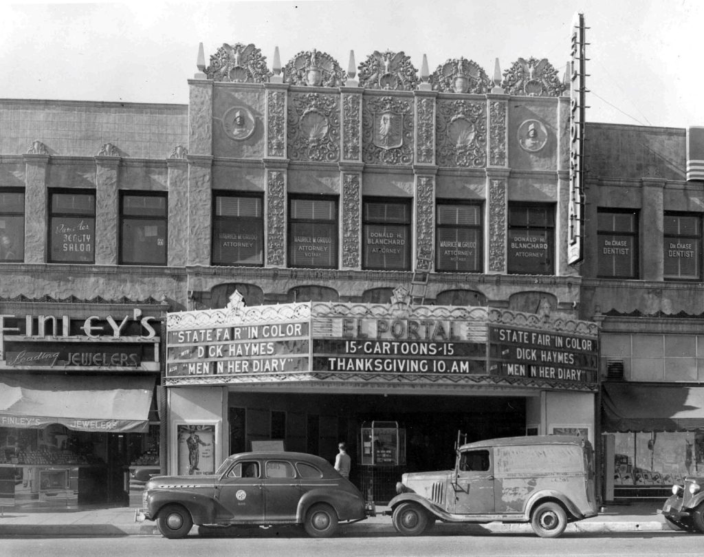 Historic black-and-white photograph of El Portal Theatre in North Hollywood, featuring its ornate Spanish Renaissance Revival facade, vintage marquee and parked cars.