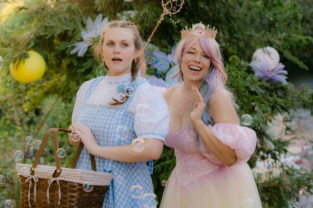 Dorothy and a pink-clad magical character pose together among bubbles during the immersive Fall Into Oz experience.