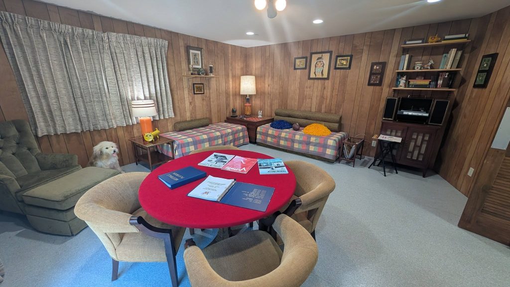 Recreated Brady Bunch family room featuring wood-paneled walls, vintage television, red round table and 1970s furnishings.