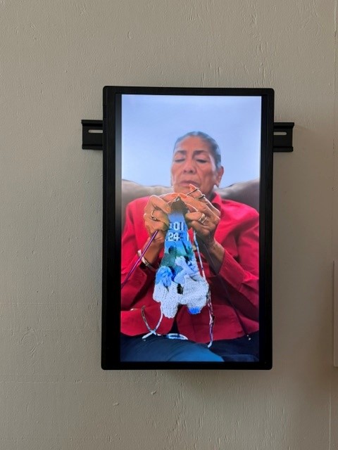 Video installation showing an older woman knitting a colorful textile, part of the Día de los Muertos art exhibition at Hollywood Forever Cemetery.