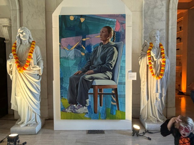 Large portrait of a seated woman displayed between two marble statues decorated with marigold garlands inside Hollywood Forever's Cathedral Mausoleum.