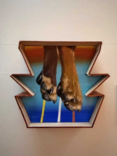 Mixed-media artwork featuring two sculpted animal hooves extending through a geometric frame against a colorful background at Hollywood Forever's art exhibition.