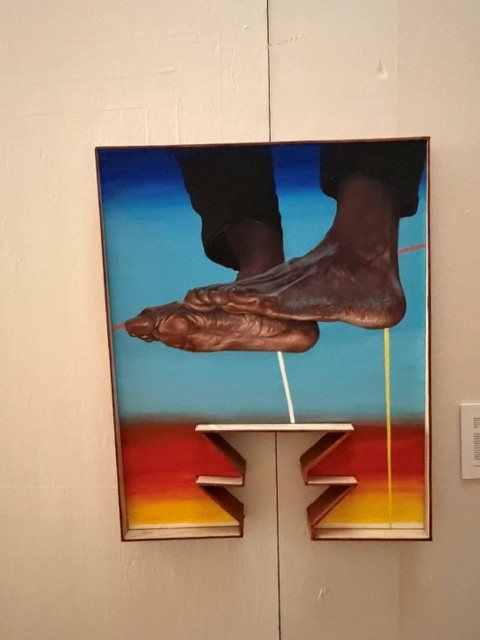 Contemporary artwork depicting a suspended human foot against a vibrant blue, orange and yellow background at Hollywood Forever's Día de los Muertos exhibition.