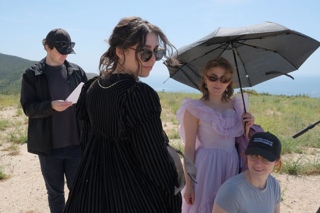 Rotation Theatre Company cast and crew working on an outdoor film shoot, with performers in period costumes and crew members reviewing production materials.