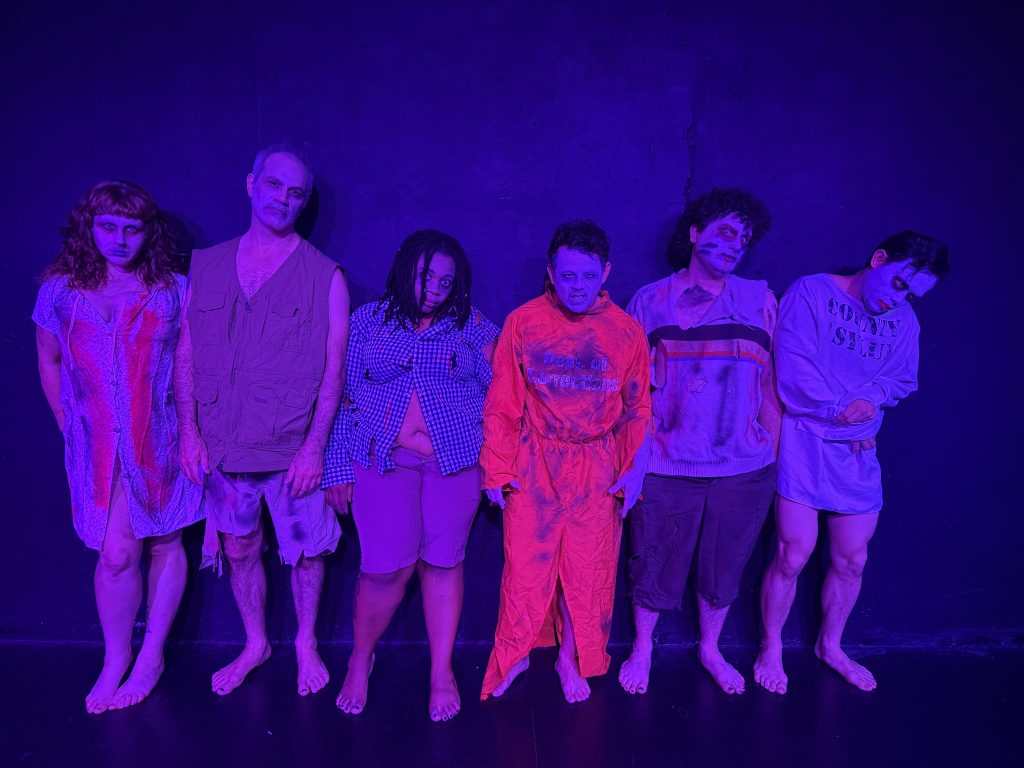 Six performers in disturbing costumes and horror makeup stand under purple lighting in Zombie Joe's Urban Death Tour of Terror ULTRA.
