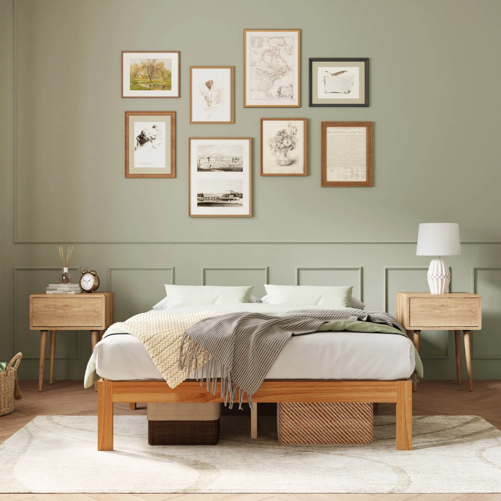 Front view of a natural wood bed frame with neutral bedding, matching wooden nightstands, sage green walls and framed artwork in a thoughtfully designed bedroom.