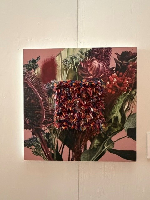 Mixed-media floral artwork featuring a textured arrangement of colorful fabric flowers over a botanical print at Hollywood Forever's Día de los Muertos exhibition.
