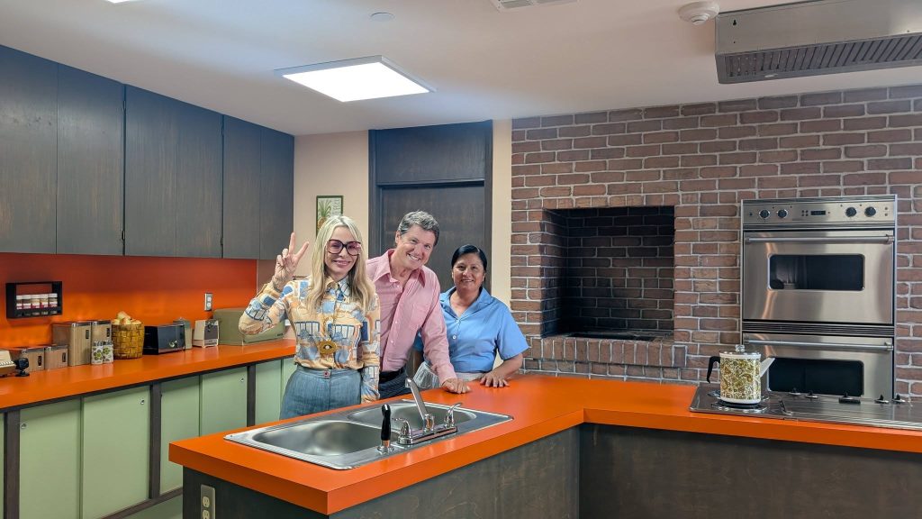 Jack Witt poses with Alison Martino and another woman in The Brady Bunch kitchen, featuring its iconic orange countertops.